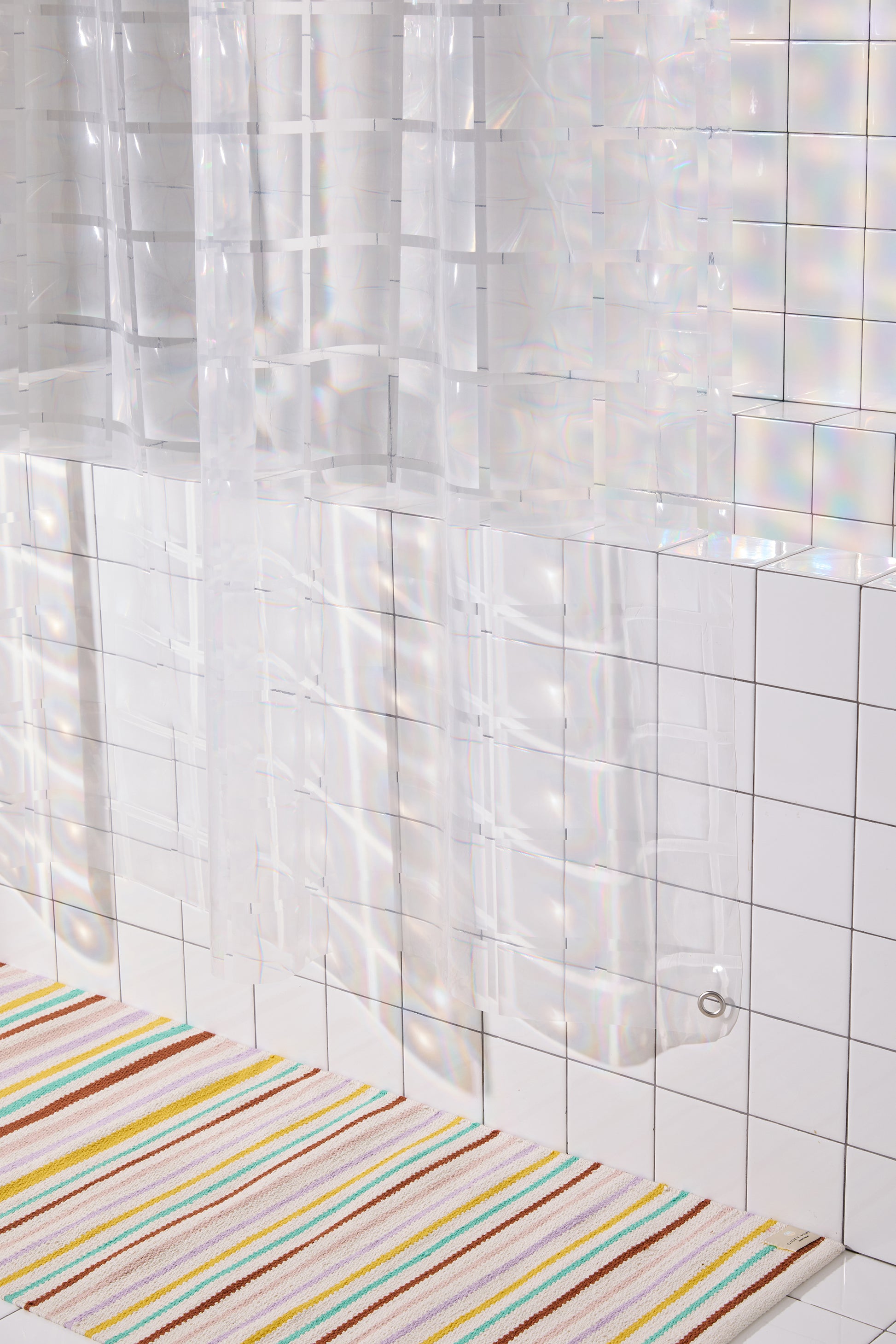 bottom corner of clear 3D curtain hanging in bathroom with white tile with colorful striped rug. 