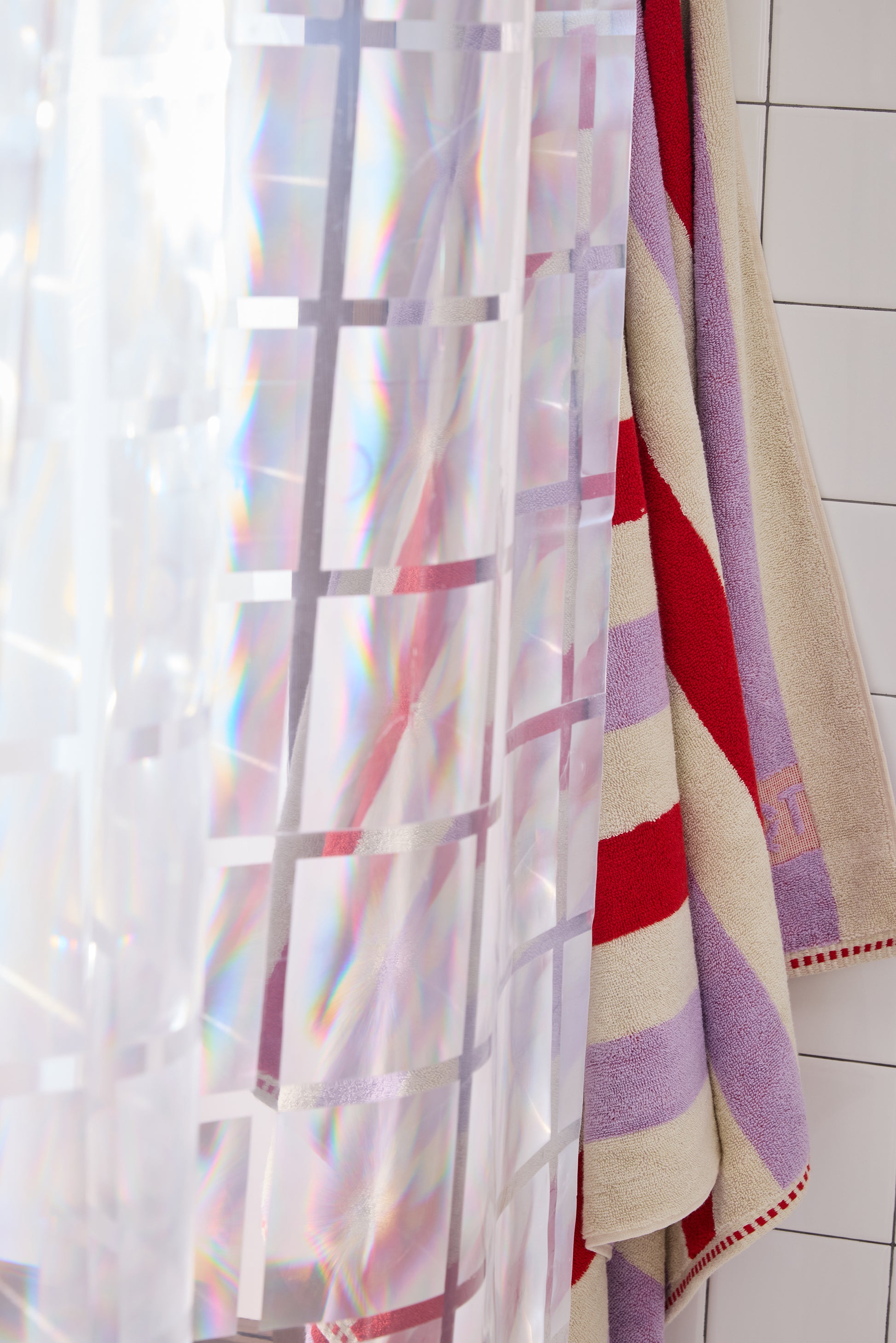 clear 3D curtain hanging in bathroom with white tile with colorful striped towel.