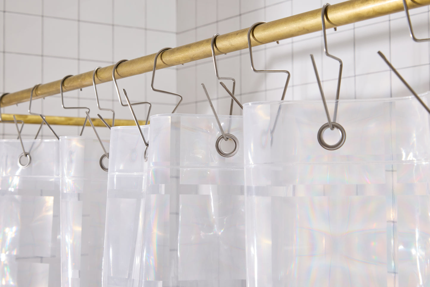 Top hem of clear 3D curtain hanging in bathroom with silver hooks on brass rod. 