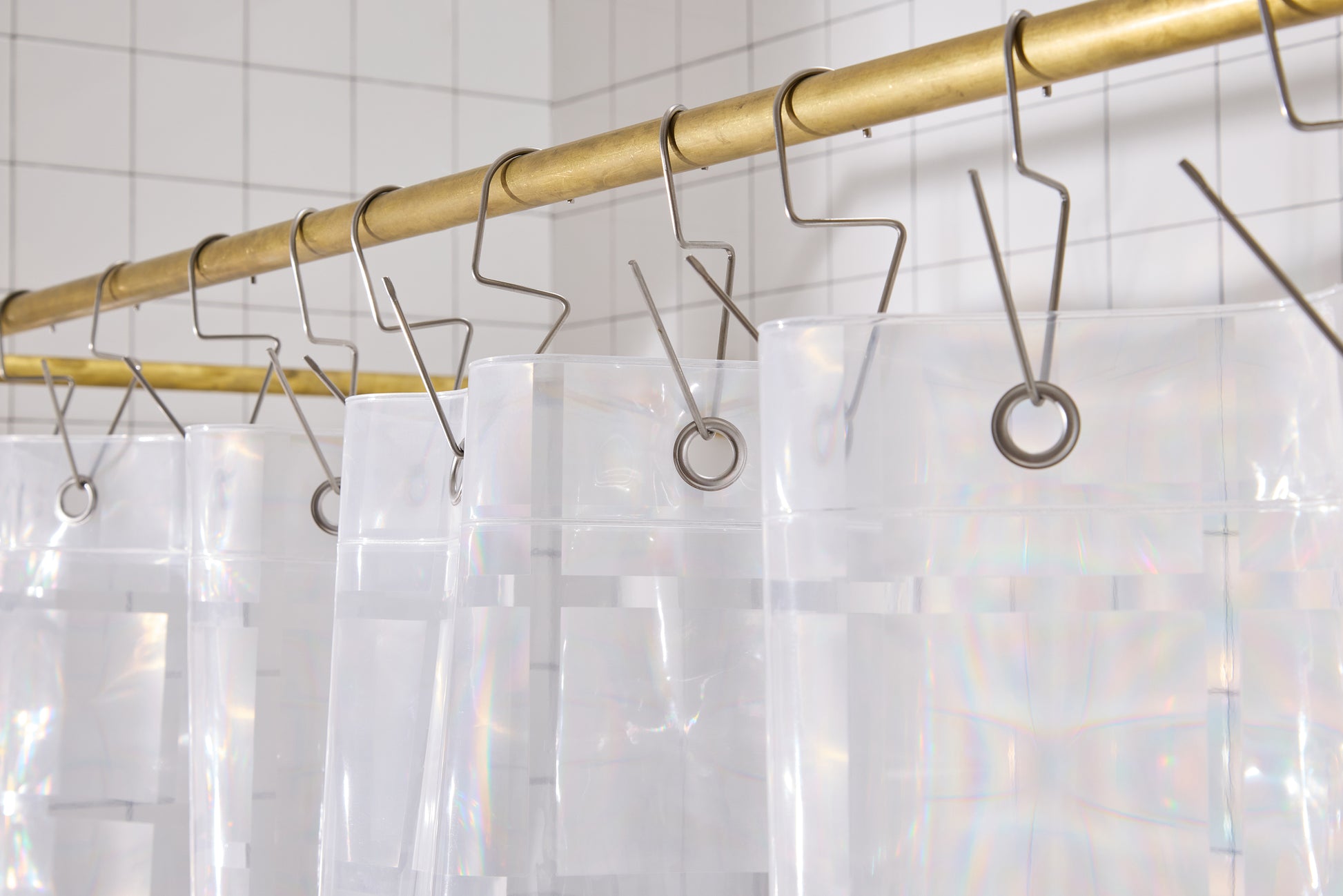 Top hem of clear 3D curtain hanging in bathroom with silver hooks on brass rod. 