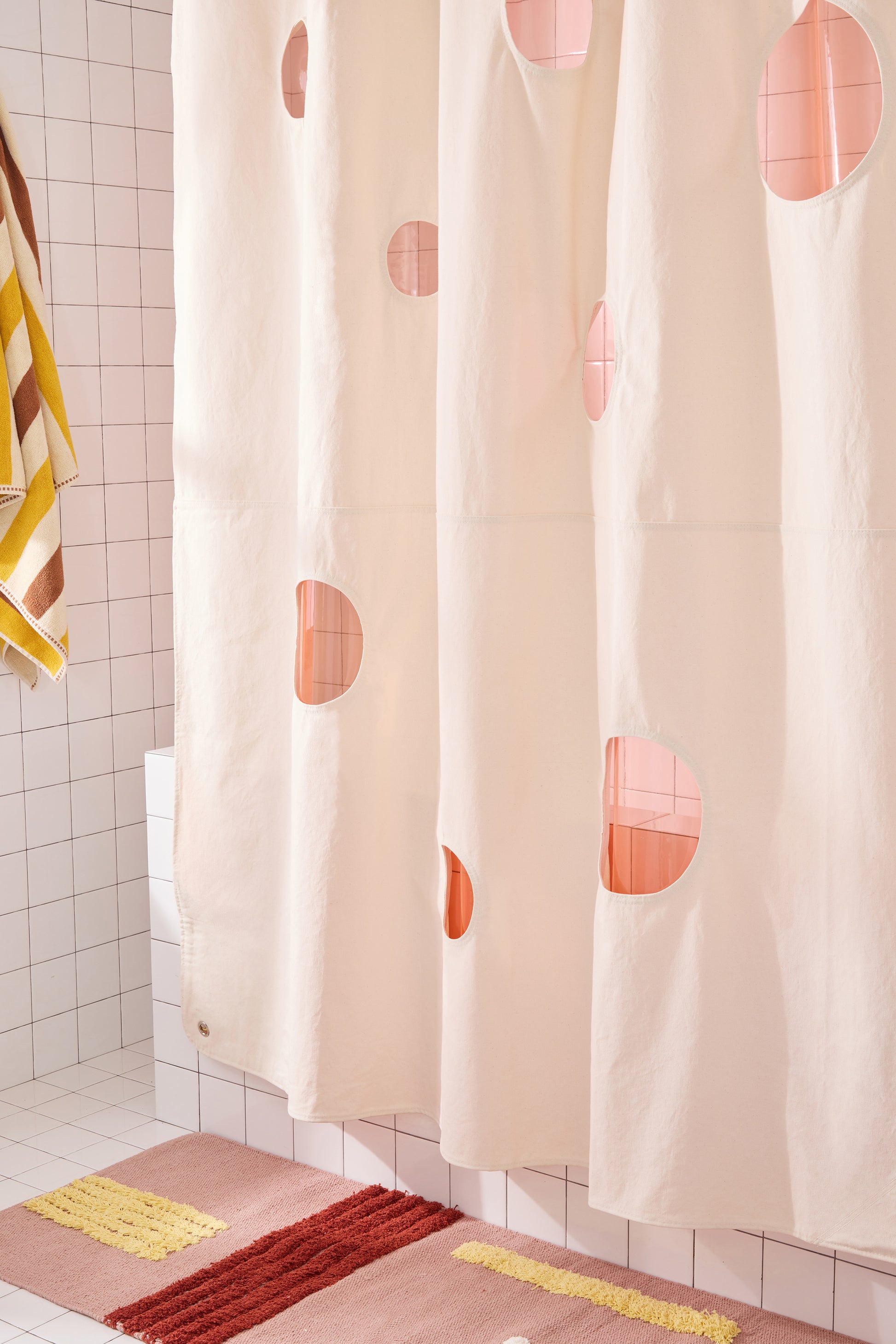 canvas curtain hanging with rose colored rug and peony sun shower curtain layered behind it. 