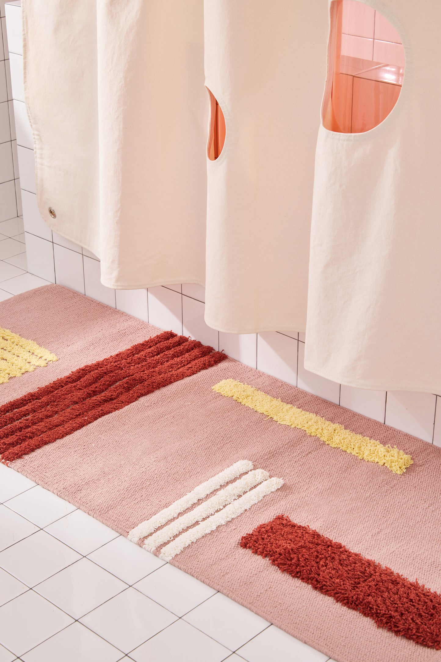 canvas curtain hanging with rose colored rug and peony sun shower curtain layered behind it. 