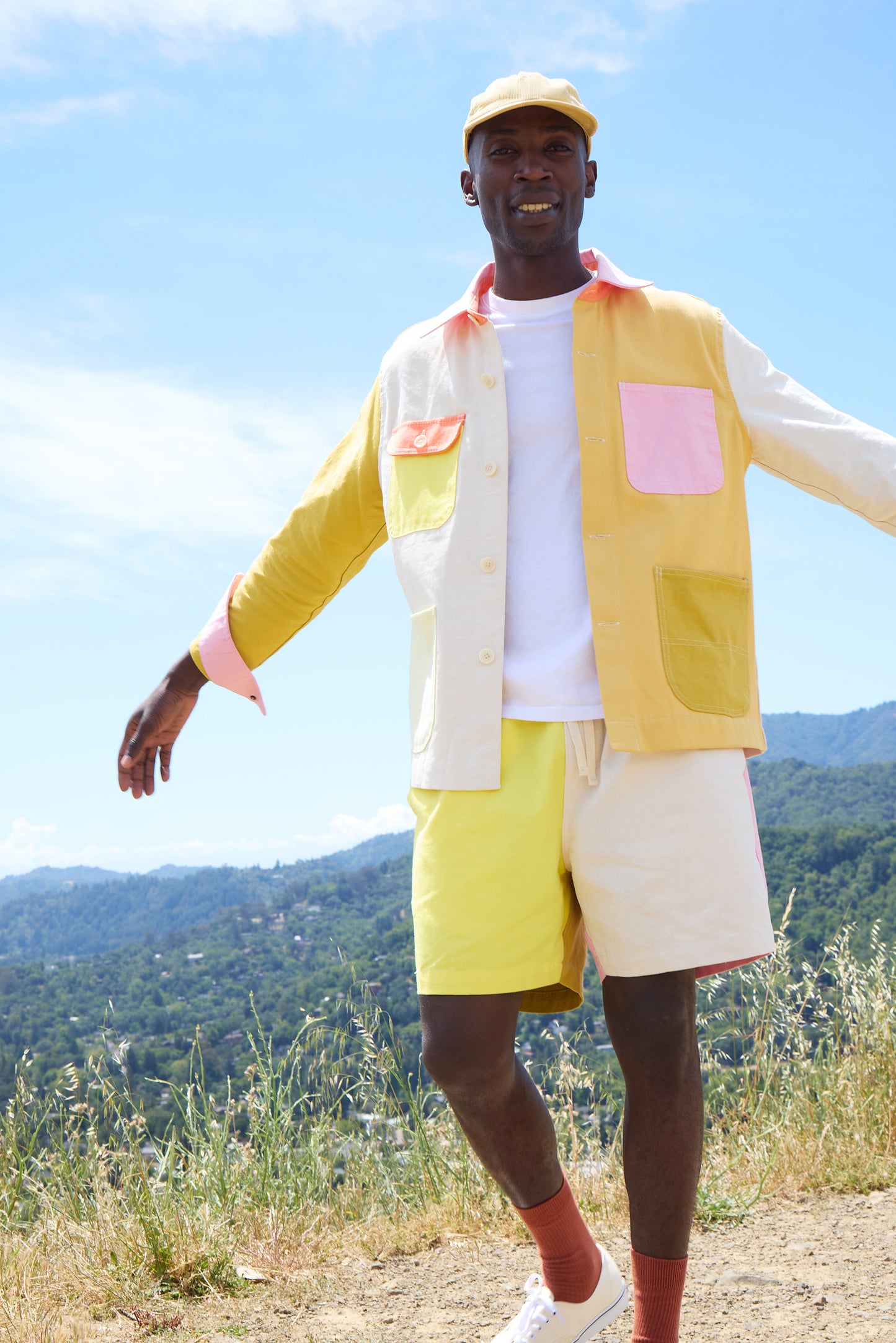 Person wearing a colorful outfit with a vest and shorts standing outdoors with mountains in the background