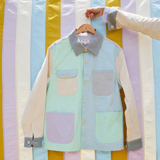 Pastel-colored color-blocked jacket with pockets on a hanger against a striped background