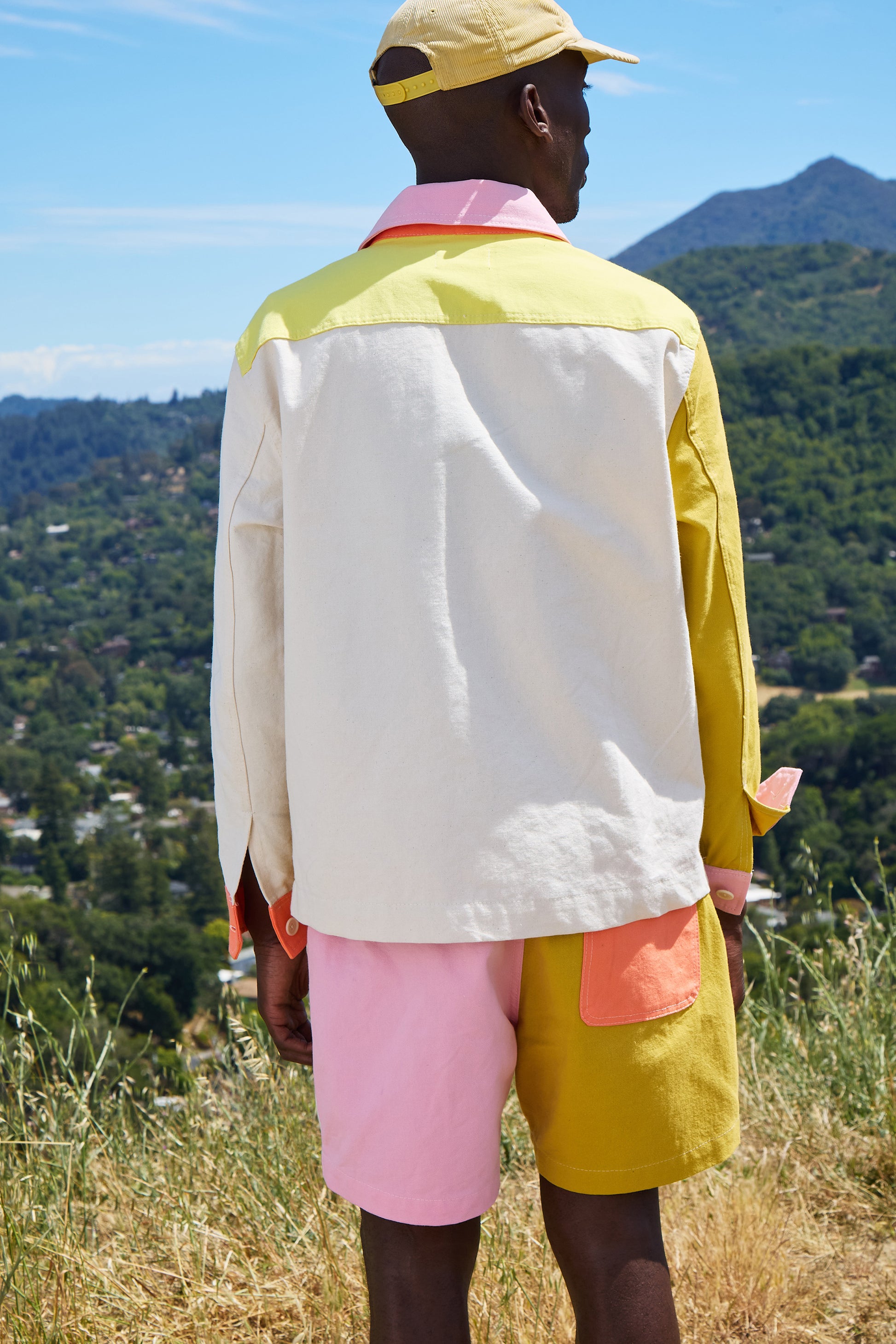 Person wearing a colorful jacket and shorts standing on a hill with a scenic view.