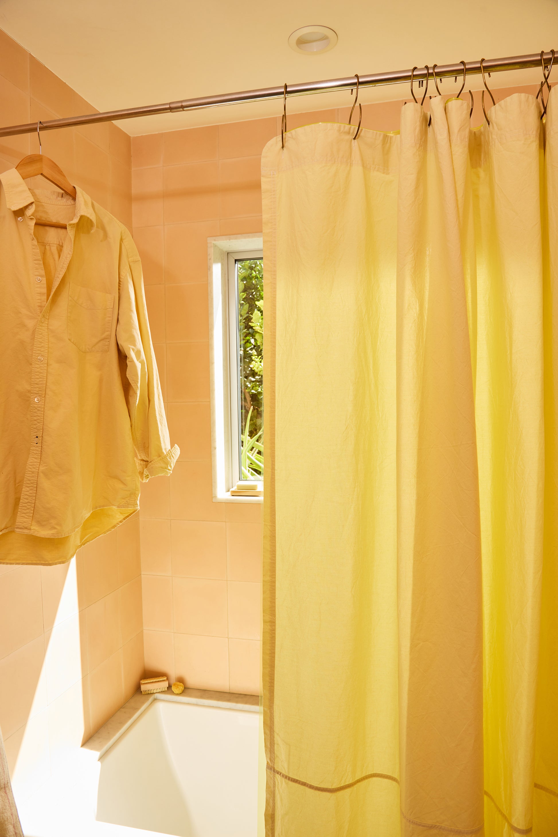 Yellow shower curtain in a bathroom with a window and hanging yellow shirt.