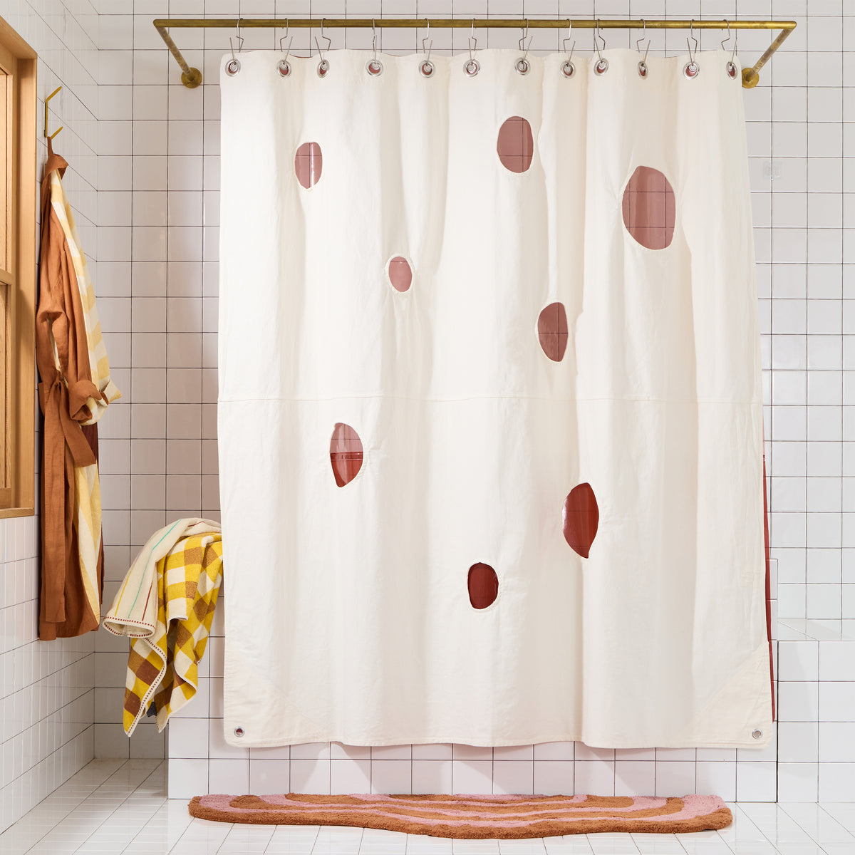 cream curtain with circles cut out and rose liner behind it on white tiled set wtih rose colored rug.