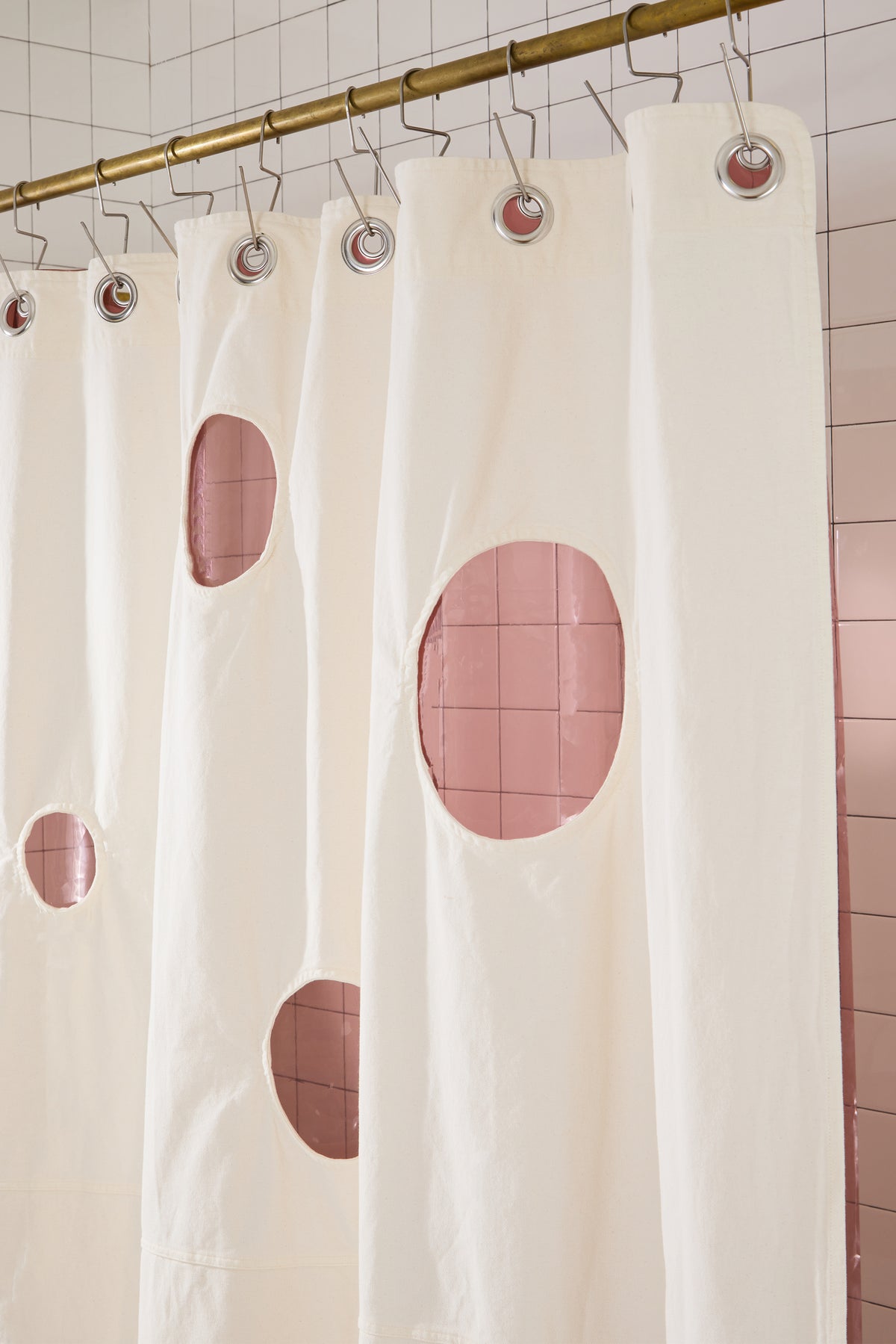 cream curtain with circles cut out and rose liner behind it on white tiled bathroom set. 