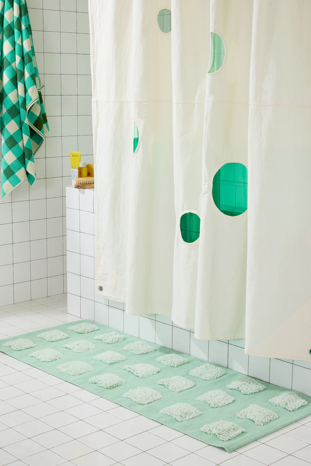 cream curtain with circles cut out and green liner behind it on white tiled bathroom set and mint green rug. 