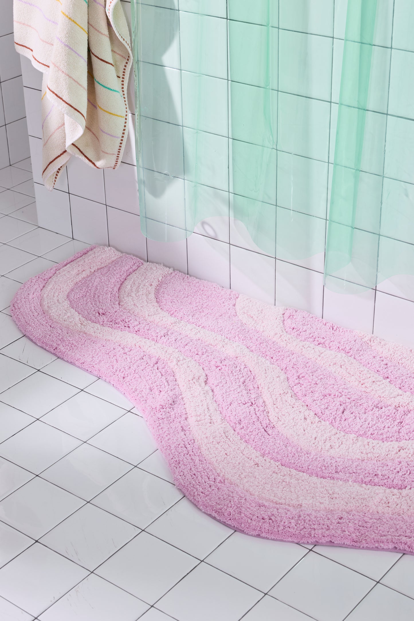Pink bath mat on a tiled bathroom floor with a shower curtain in the background.