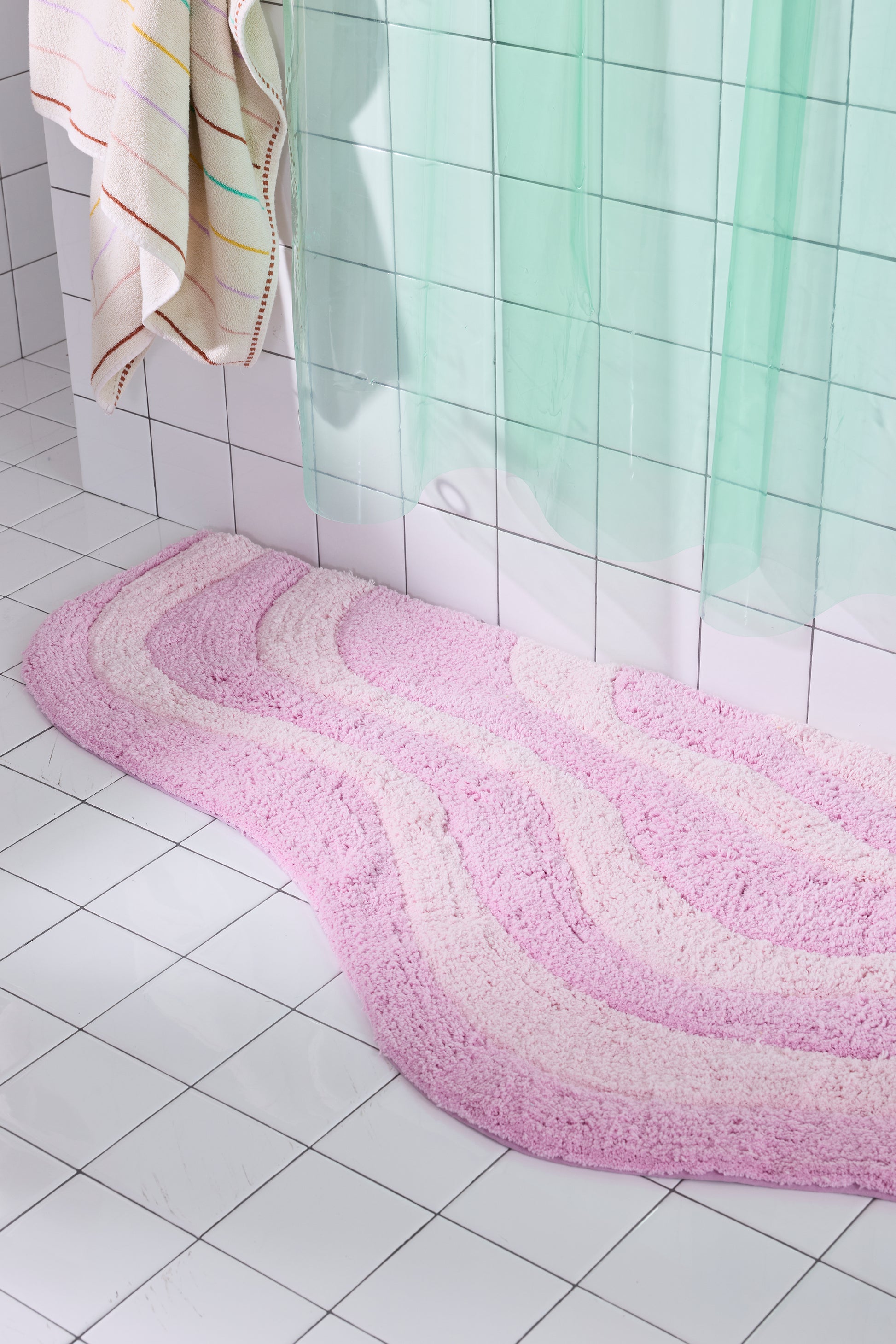 Pink bath mat on a tiled bathroom floor with a shower curtain in the background.
