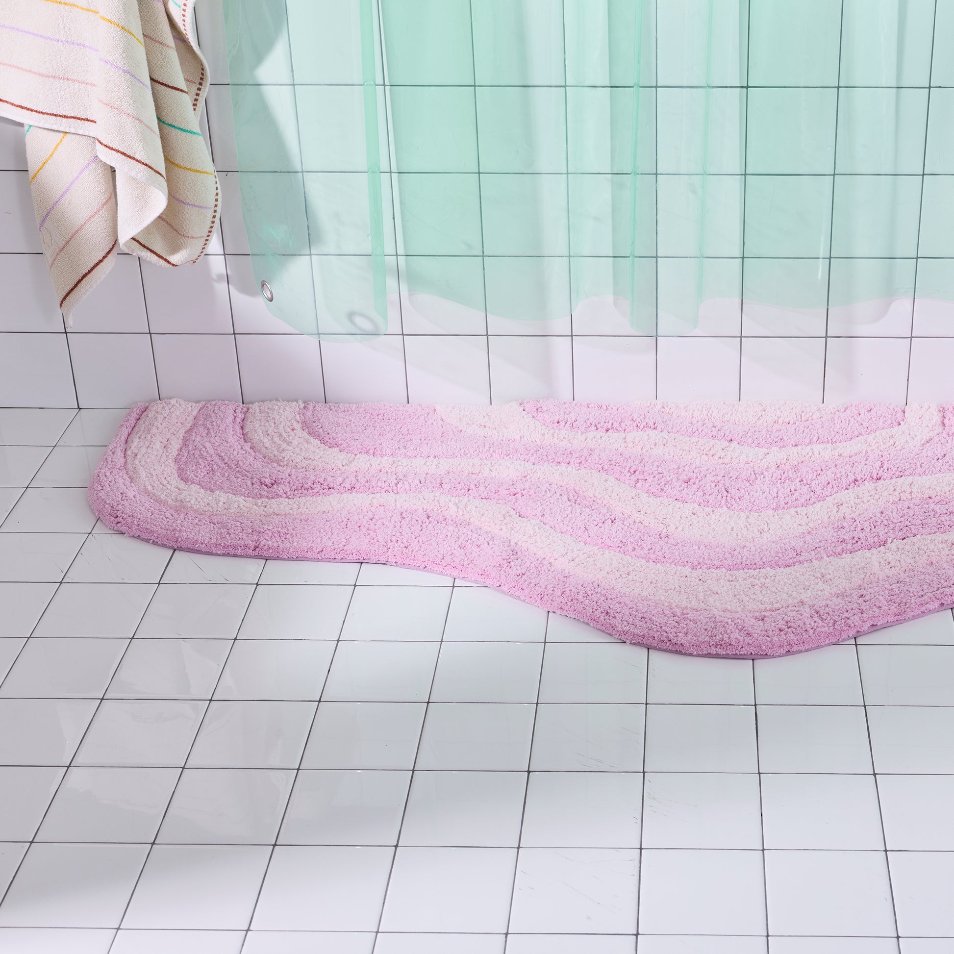 Pink bath mat on a tiled bathroom floor with a shower curtain in the background.