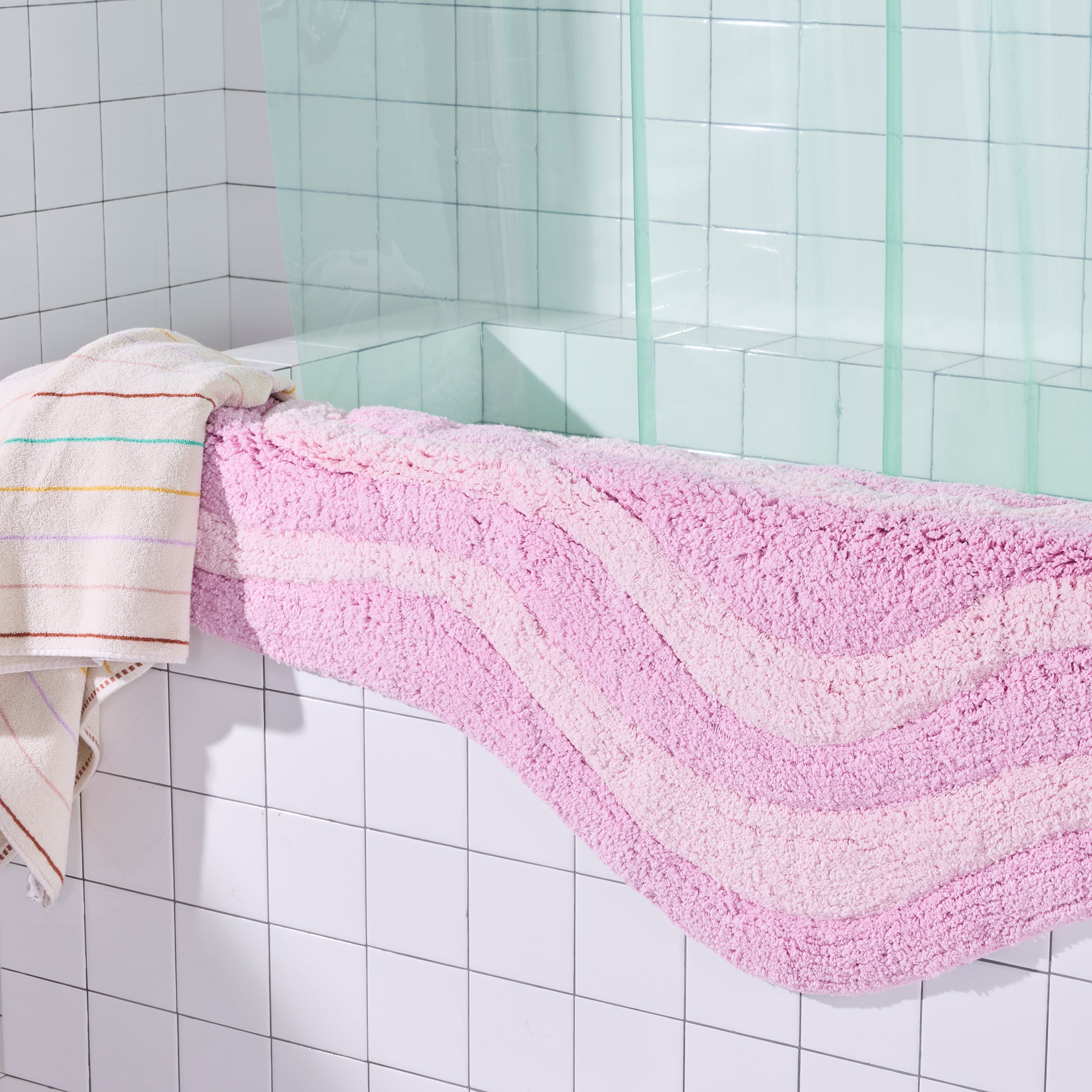 Pink bath mat with wavy pattern on a tiled bathroom floor