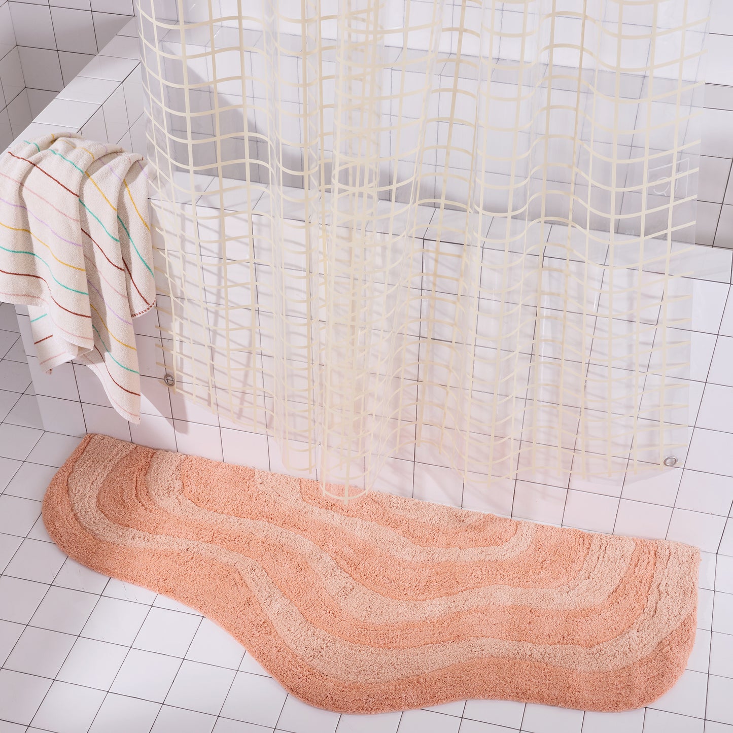 Peach wavy Bath mat on a tiled bathroom floor with a shower curtain in the background