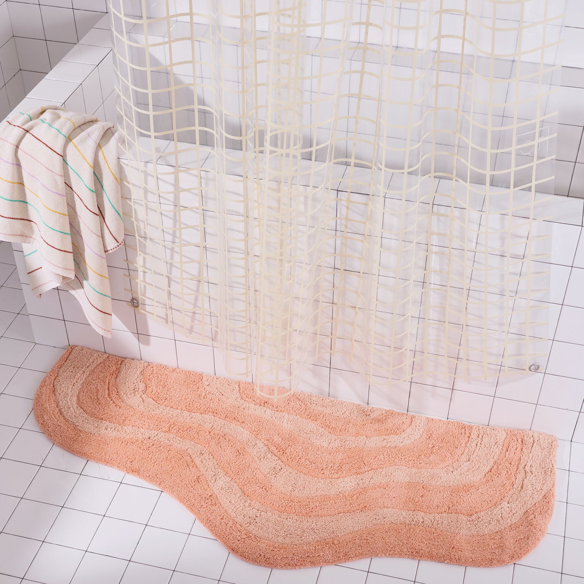 Peach wavy Bath mat on a tiled bathroom floor with a shower curtain in the background