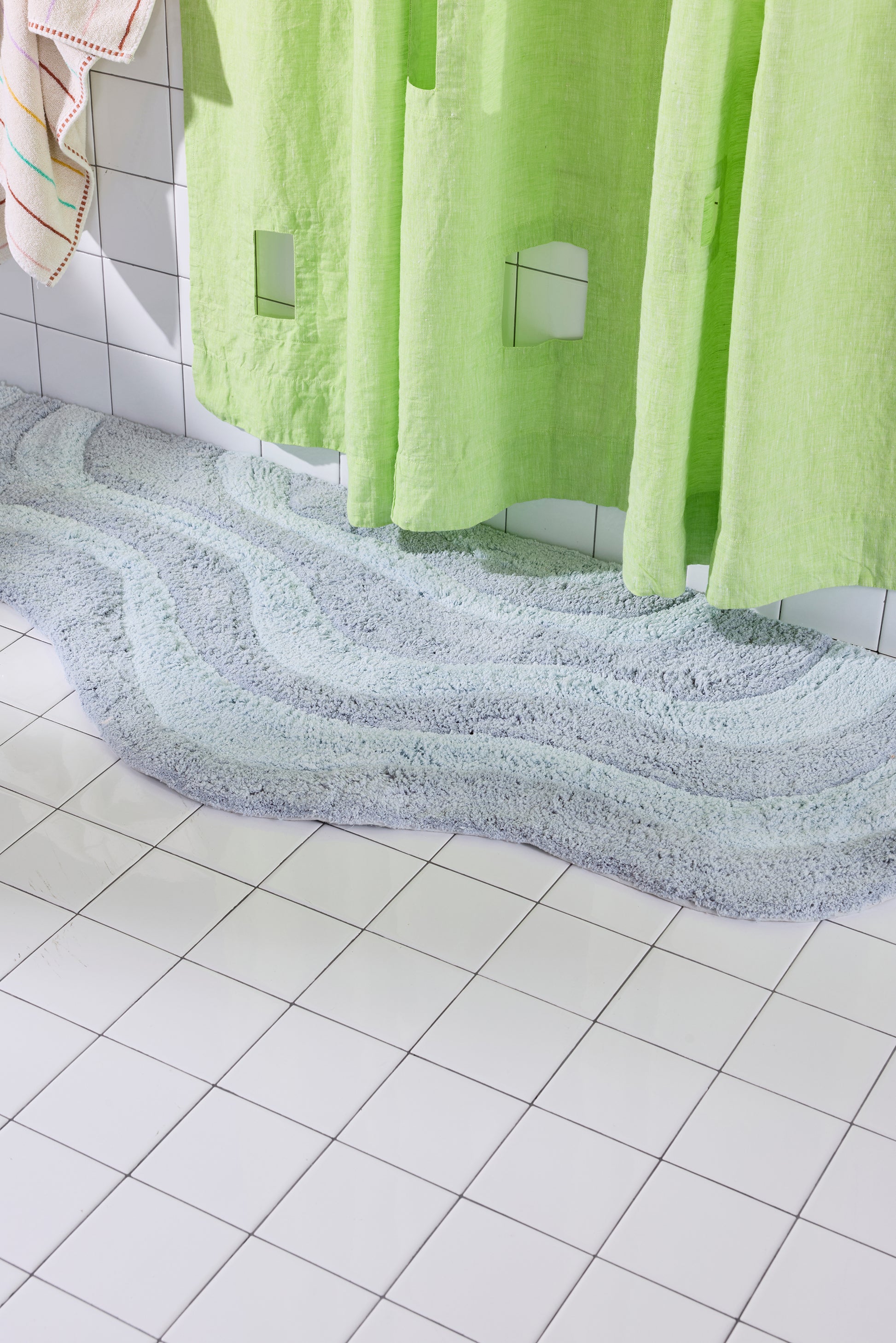 Green shower curtain with a textured floor and tiled wall in the background