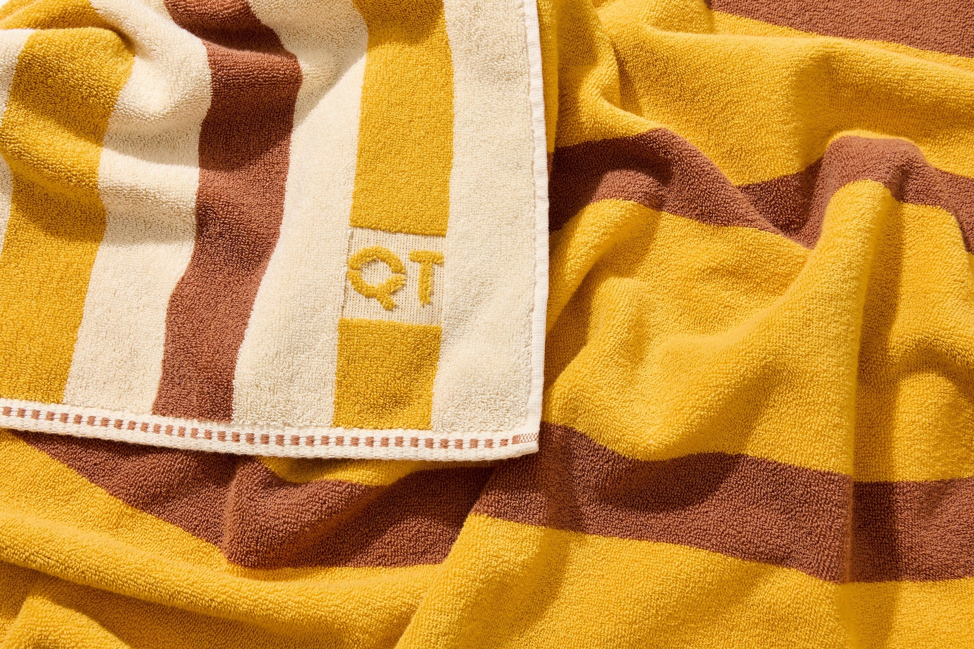 Corner detail of catalina bath sheet in canyon featuring embossed QT logo. 