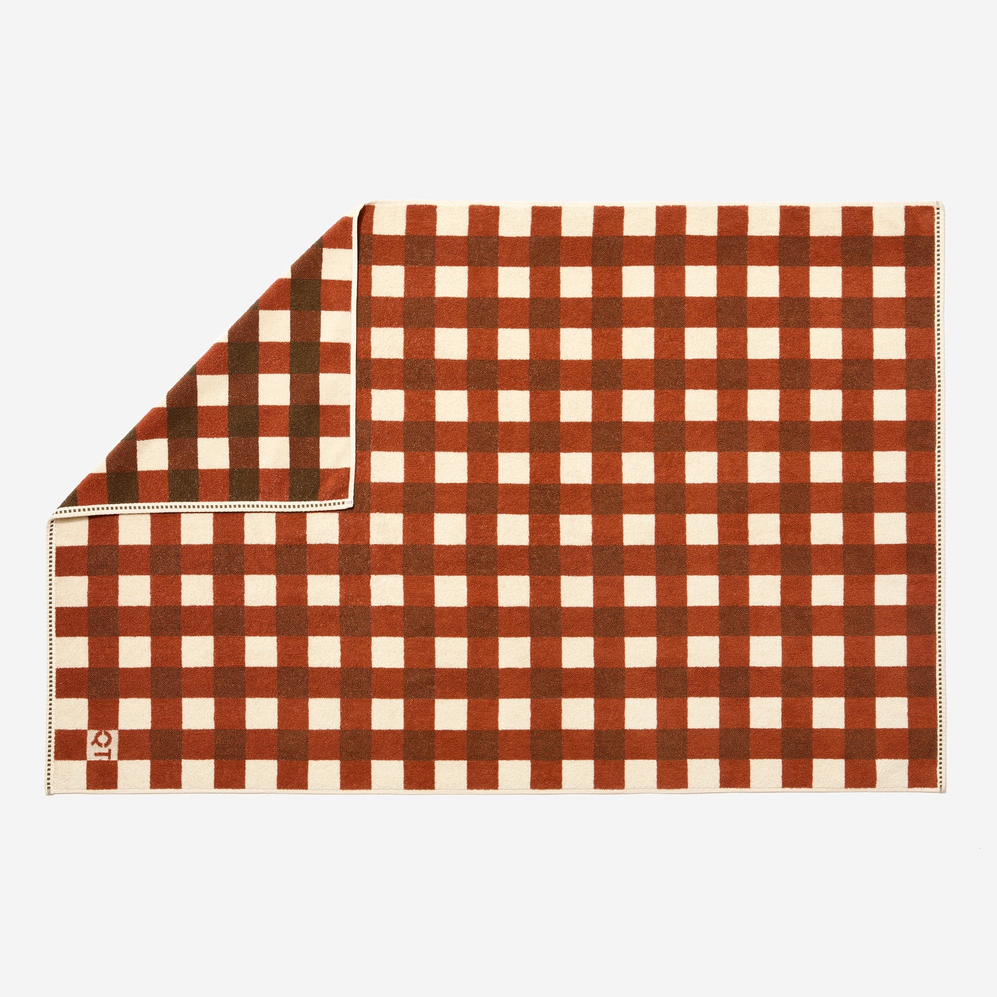 Full view of tam bath sheet in chocolate laid out, one corner flipped up to detail more saturated side of pattern. 