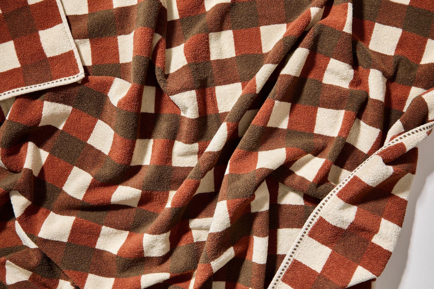 Detail view of tam bath sheet scrunched up showing clay, chocolate and cream checks.