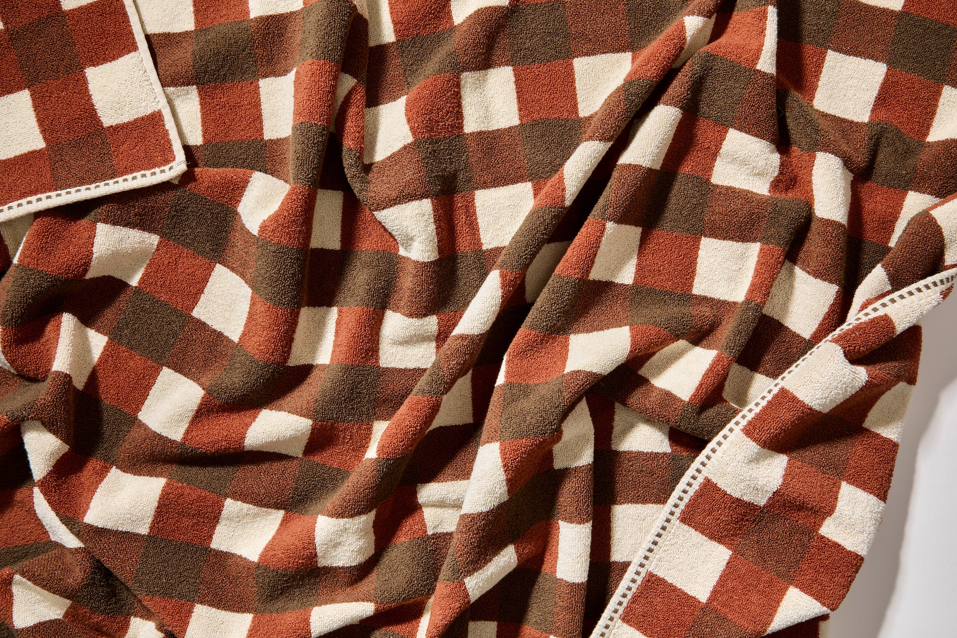Detail view of tam bath sheet scrunched up showing clay, chocolate and cream checks.