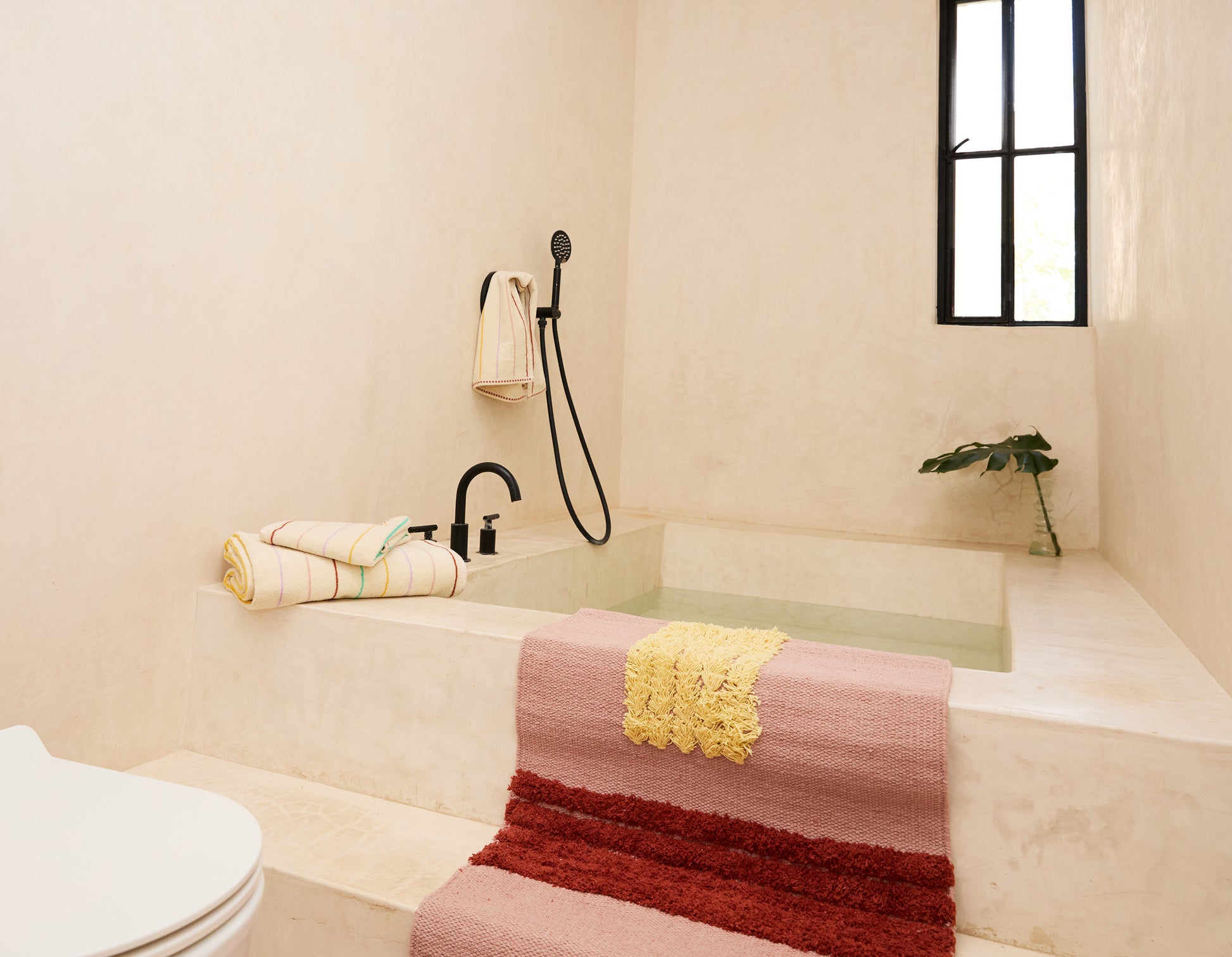 rose colored Reyes rug in a bathroom, laying over steps to tub, with striped towels 
