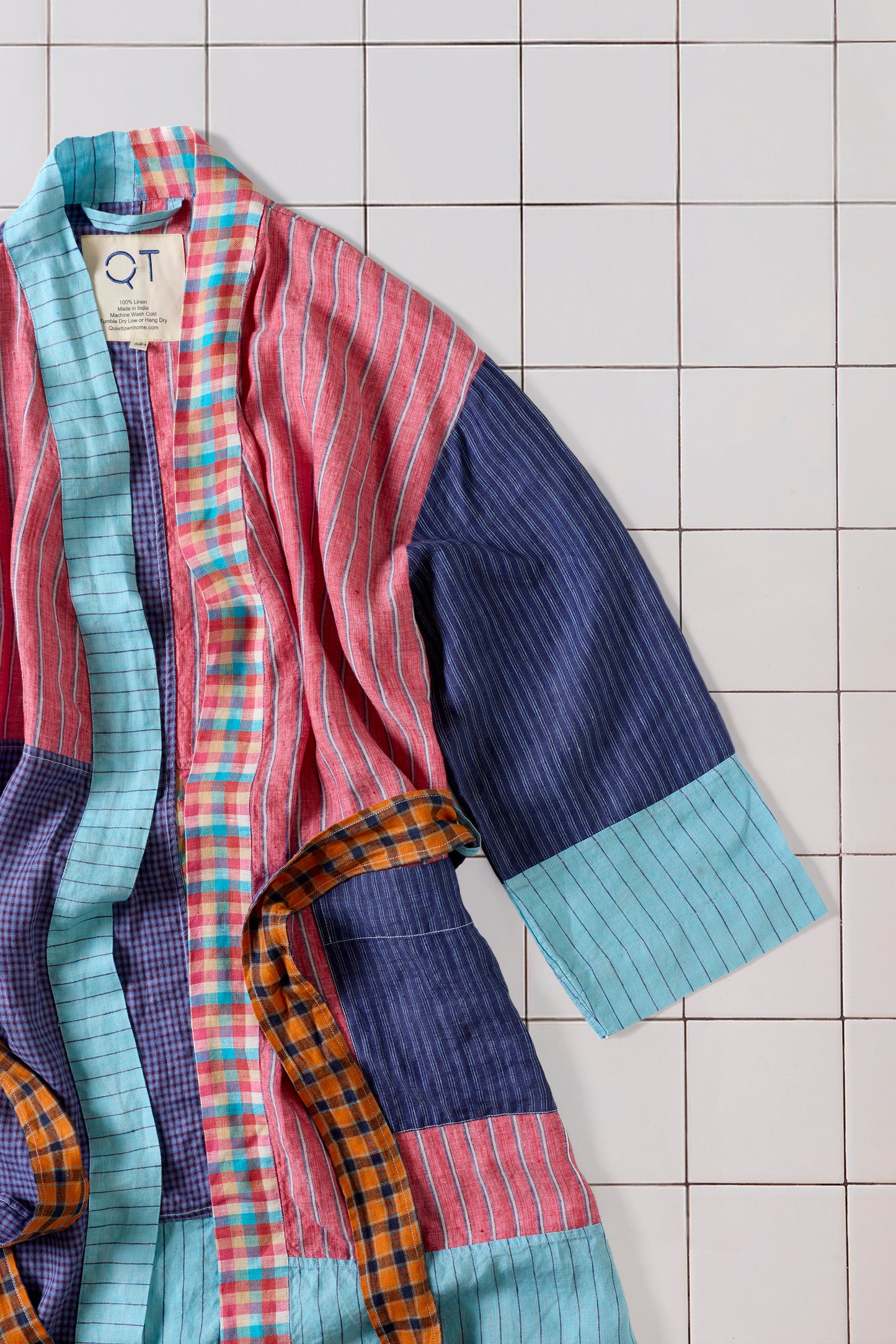 Colorful patchwork robe with plaid patterns on a tiled floor, featuring a QT label.