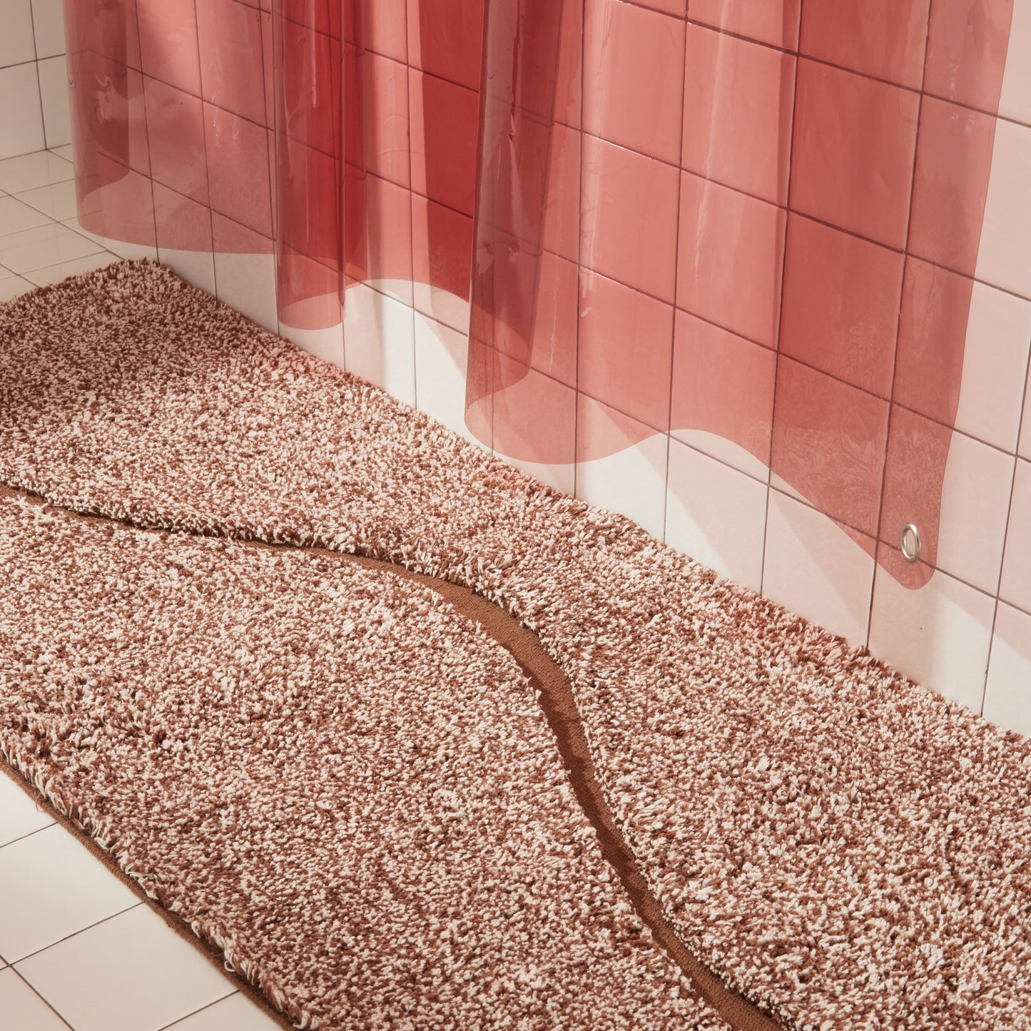 Brown bath mat in 56"x22" size with curvy path stripe contrast shot styled in a white tiled bathroom next to rose colored sun shower curtain.