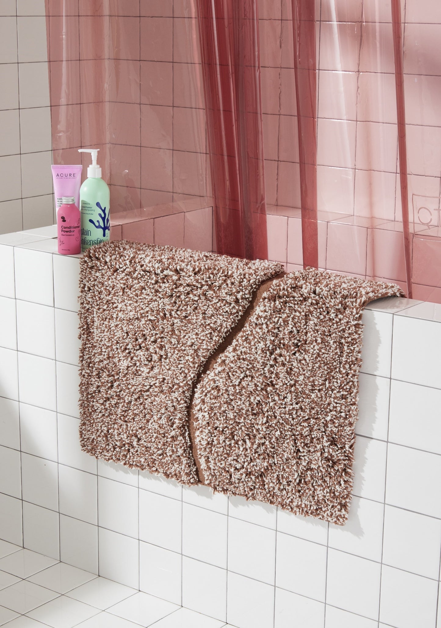 Brown bath mat in 21"x31" size with curvy path stripe contrast shot laid over the side of white tiled bathtub.