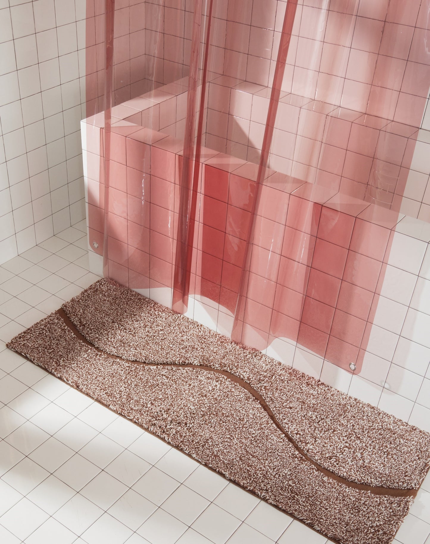 Full view of brown bath mat in 56"x22" size with curvy path stripe contrast shot styled in a white tiled bathroom next to rose colored sun shower curtain.