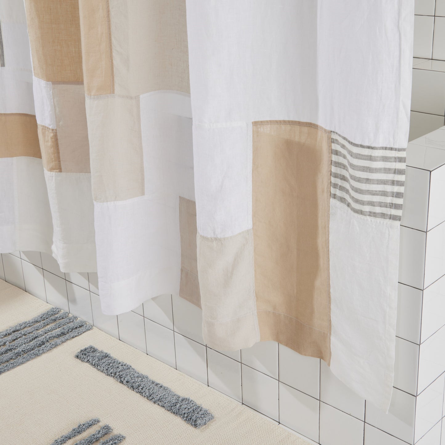 Bottom view of multi color linen shower curtain in sand hangs above reyes bath mat in storm.