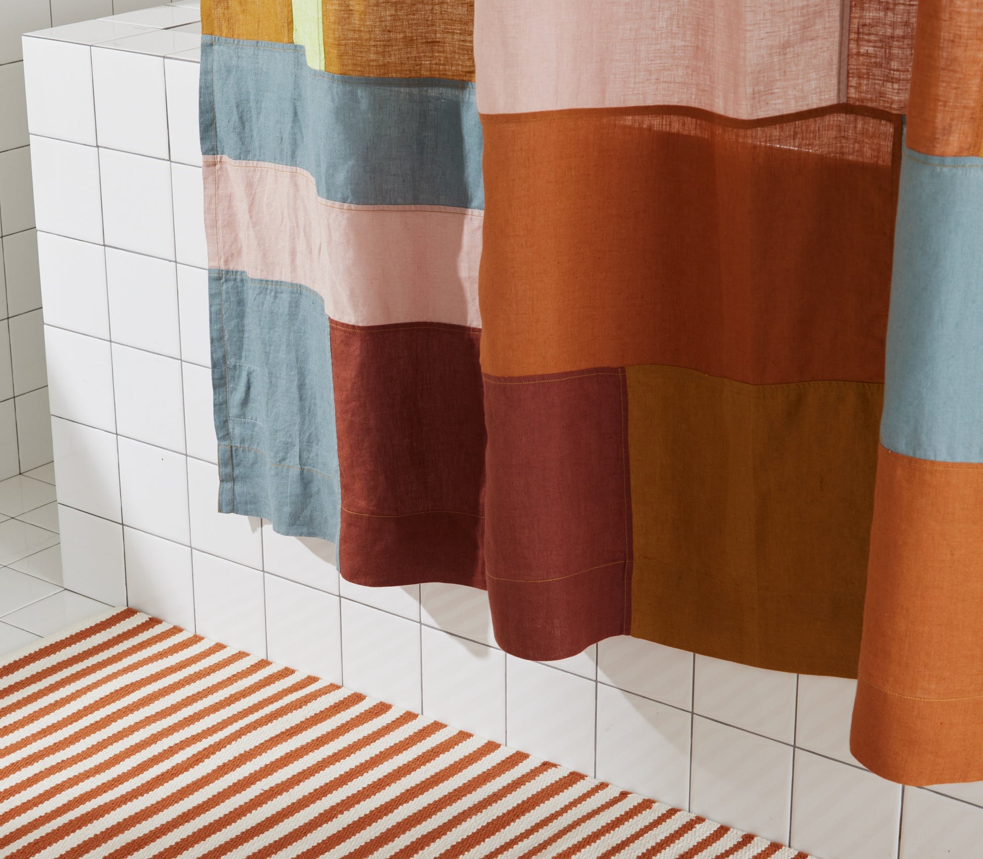 Detail of bottom view of multi-color linen shower curtain in rose styled above the ojai bath mat in clay. 