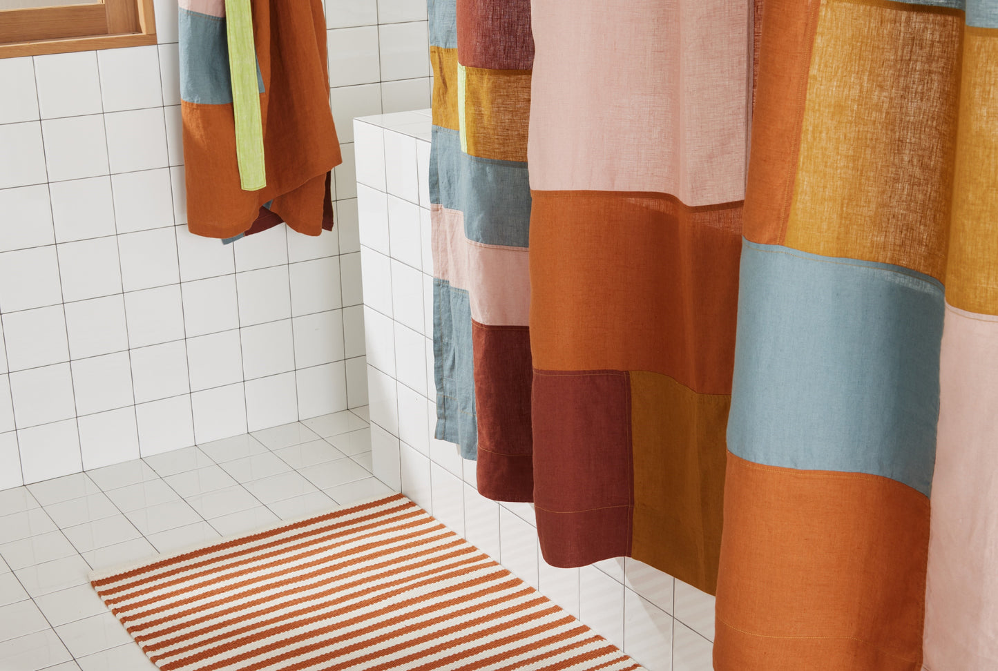 Bottom view of multi-color linen shower curtain with warm-toned patchwork pattern styled above the ojai bath mat. 
