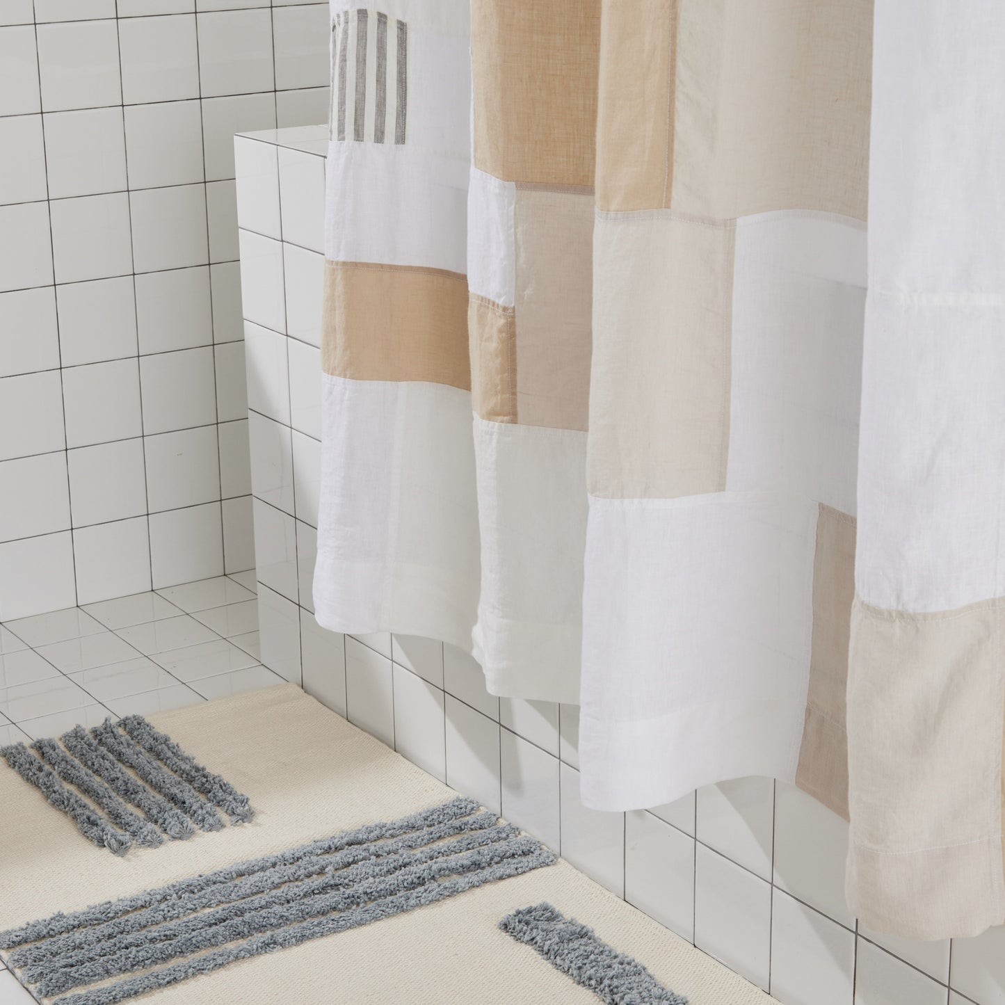 Bottom view of multi-color linen shower curtain in sand styled above a reyes bath mat in storm. 