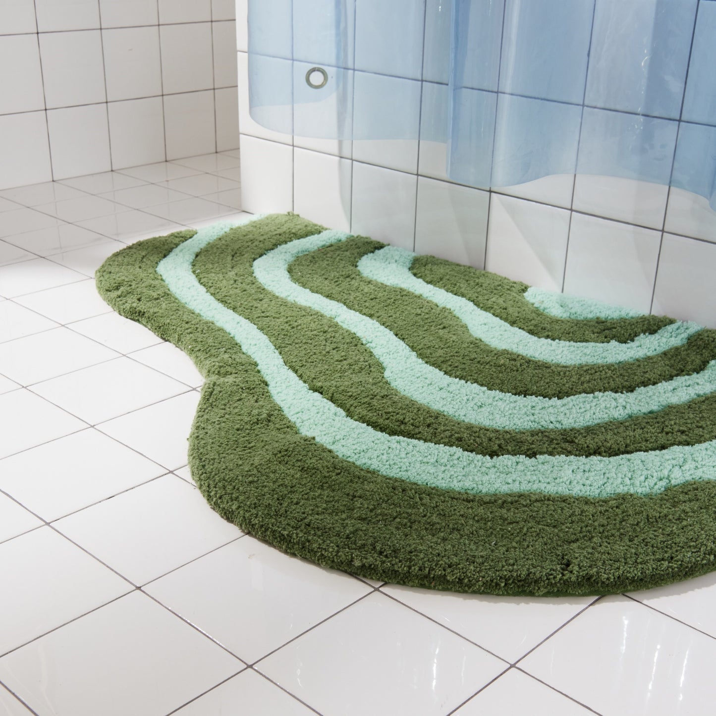 Side view of pine and jade striped, lost coast rug sitting beside white tiled bathtub. 