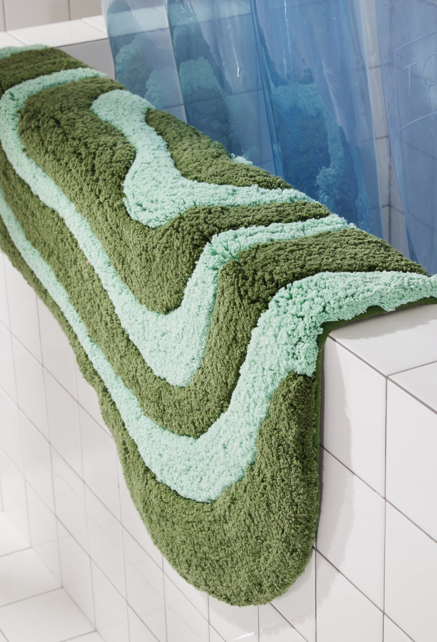 Side view of pine and jade striped lost coast bath mat laying over side of white tiled bathtub. 
