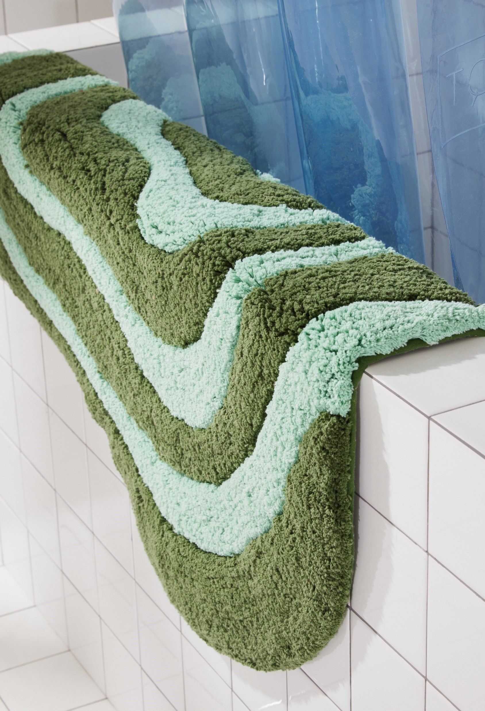 Side view of pine and jade striped lost coast bath mat laying over side of white tiled bathtub. 