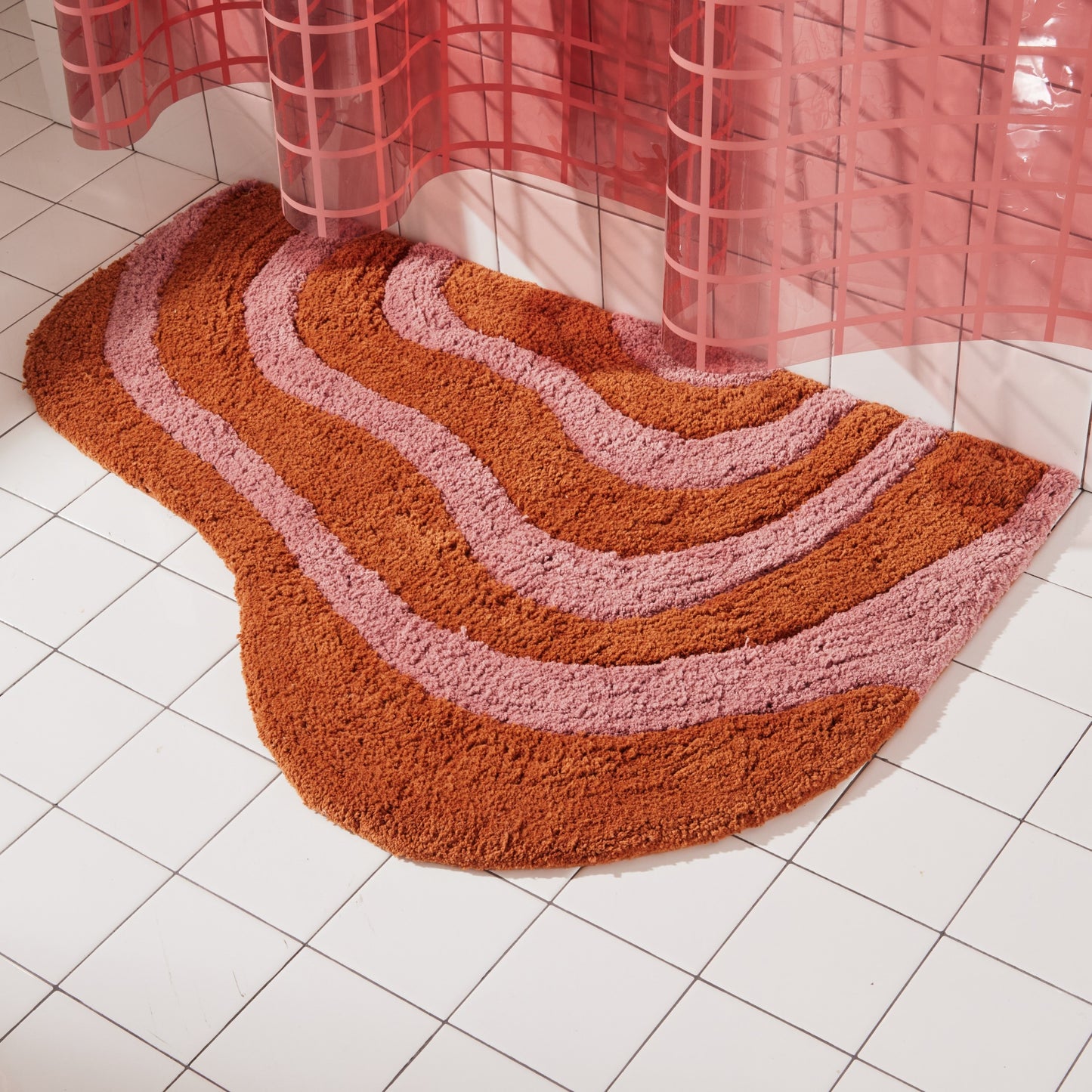 Honey and rose bath mat in 21"x31" size sitting next to white tiled bathtub styled below 2x2 sun shower in rose. 
