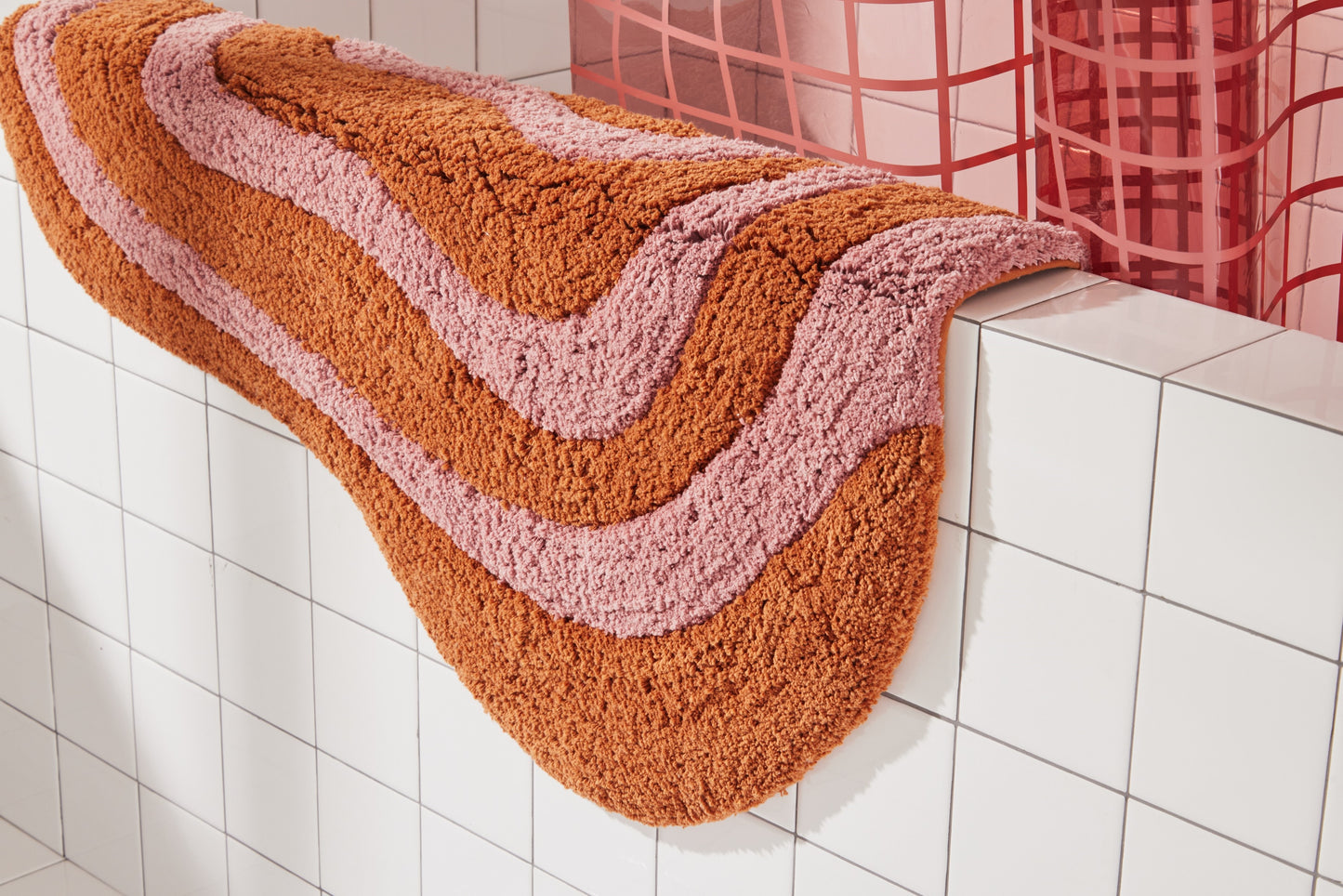 Honey and rose bath mat hanging over side of white tiled bathtub styled with 2x2 sun shower in rose. 