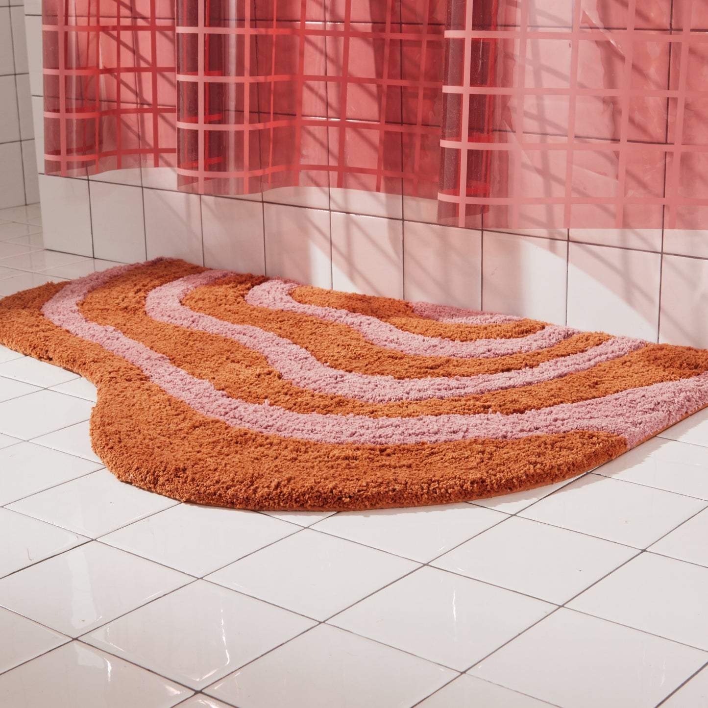 Side view of honey and rose striped, lost coast rug sitting beside white tiled bathtub. 