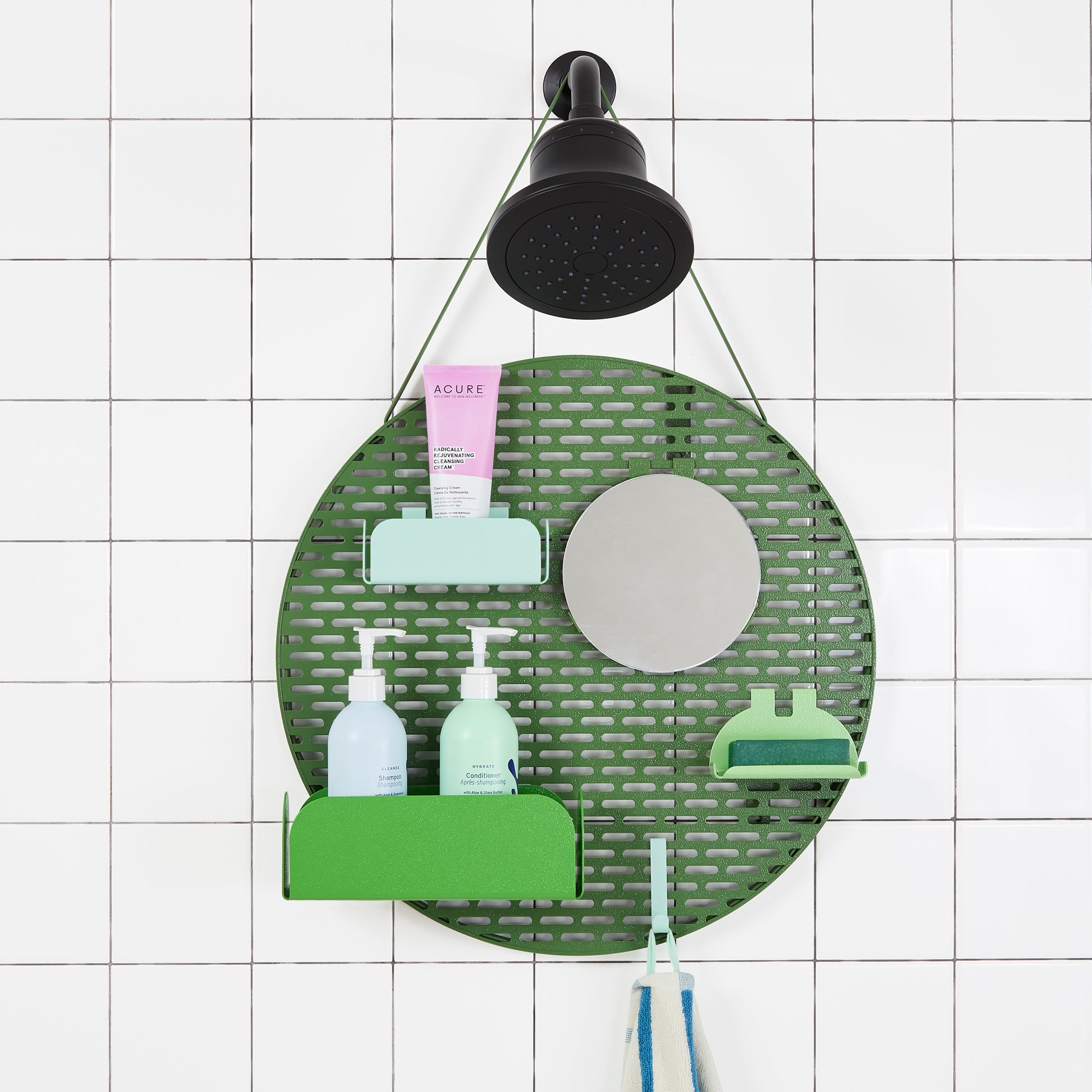 The Spot in Pine (green) hanging from a black shower head on a white tiled wall. 