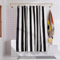 Black and white striped shower curtain in a bathroom with a towel and rug.