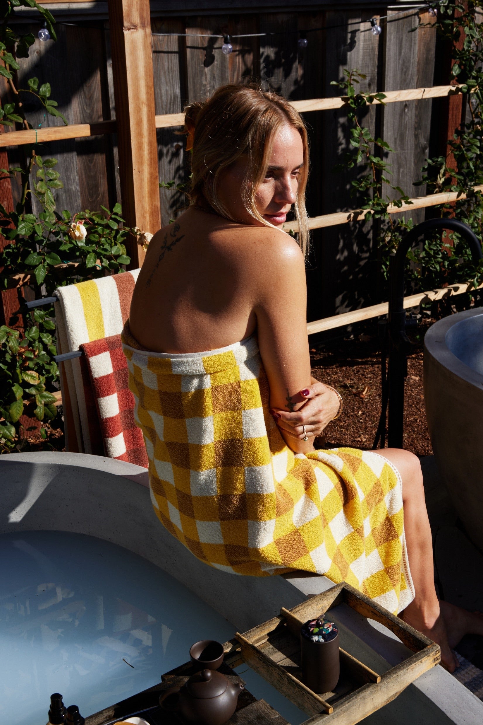 Model wears tam bath sheet in canyon in outdoor bath setting. 